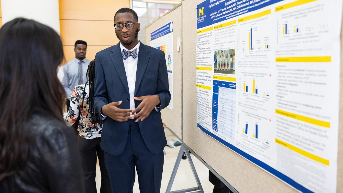 Black male student wearing navy suit and bowtie presenting a poster