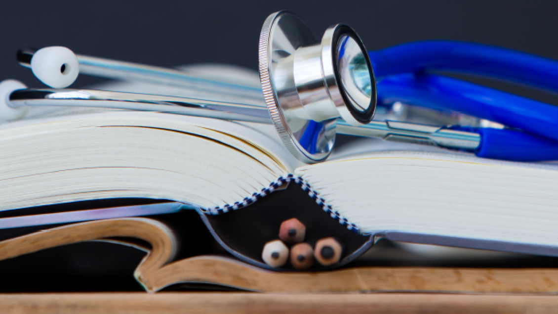 Close up image of an open book with a blue stethoscope resting on it. 
