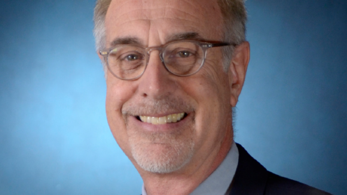 Professional portrait of a middle aged white man wearing glasses and a suit.