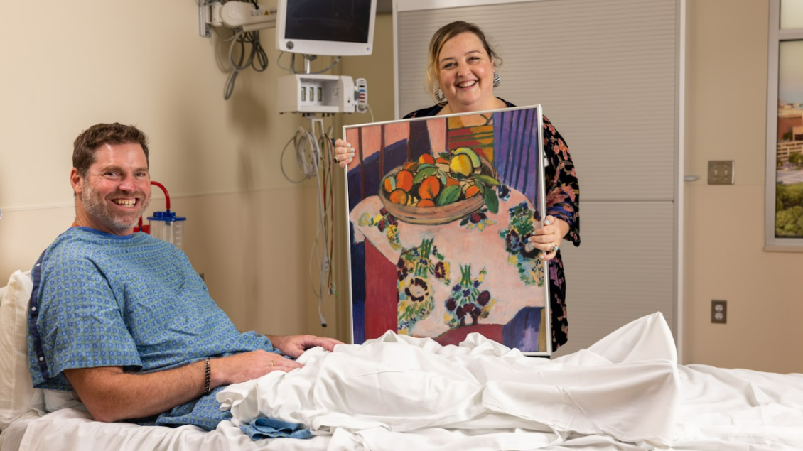 A volunteer shows an Art Cart Poster and a patient smiles