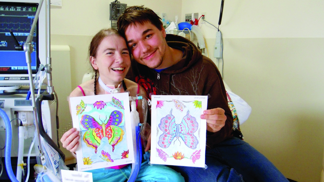 Young man and girl smiling and holding up art in hospital room