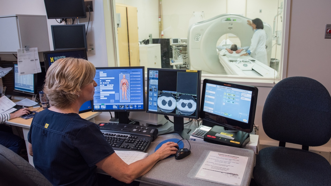 radiologist reviewing scan images as patient in the next room is being prepped for scanning