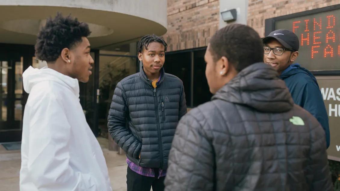 Four young black men talk outside a building