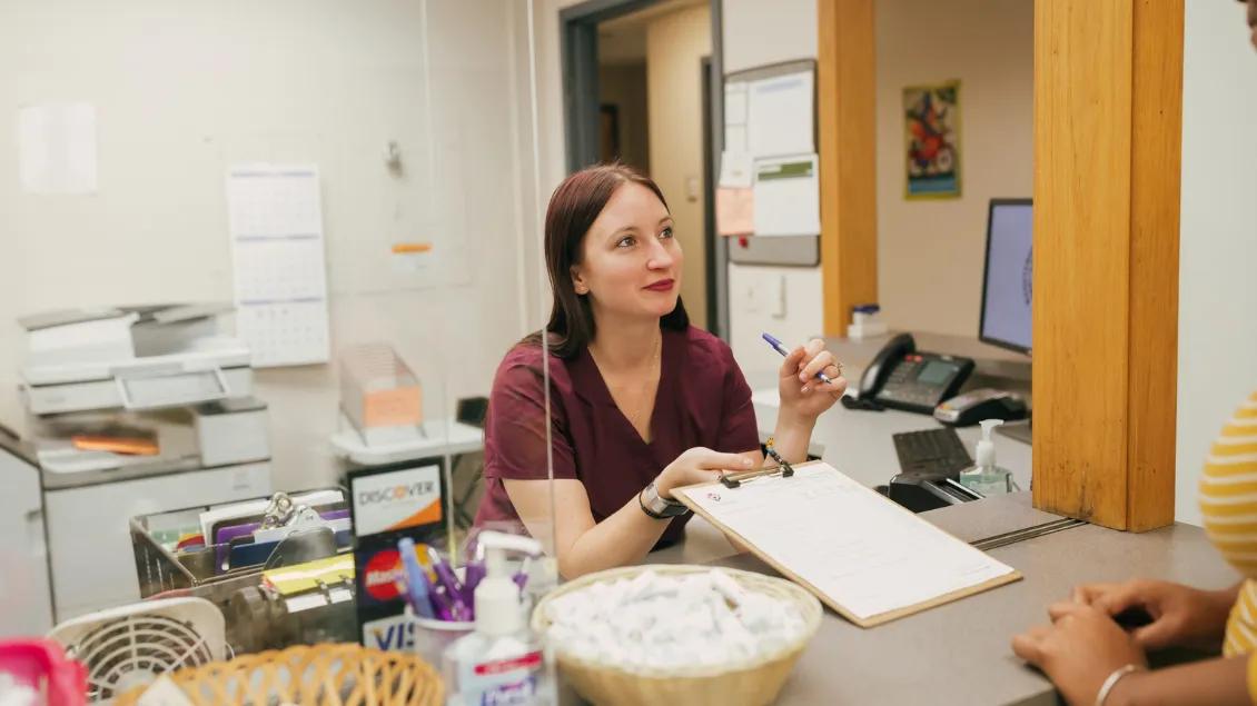 young woman holds clipboard for person at sign-in