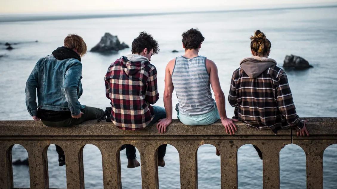 Group of young people sitting on guardrail near a river.