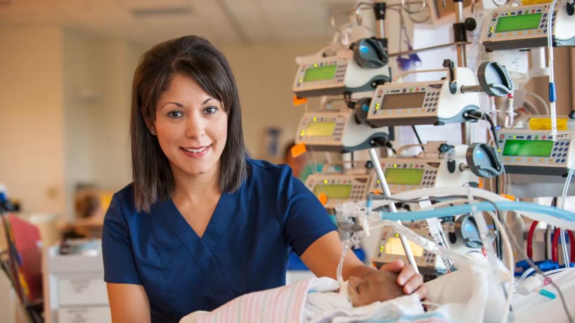 Nurse caring for an infant wrapped in blue and pink striped blankets.