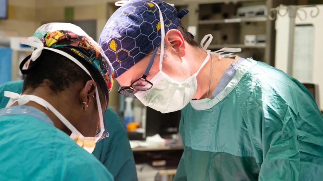 Two surgeons working in an operating room. They are wearing masks and blue scrubs.