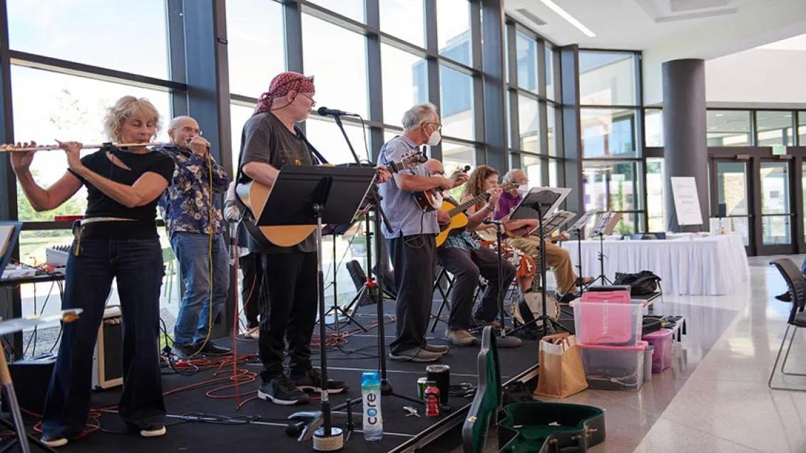 A small band including flute, five guitars, and a vocalist perform on an elevated platform in a large event space.