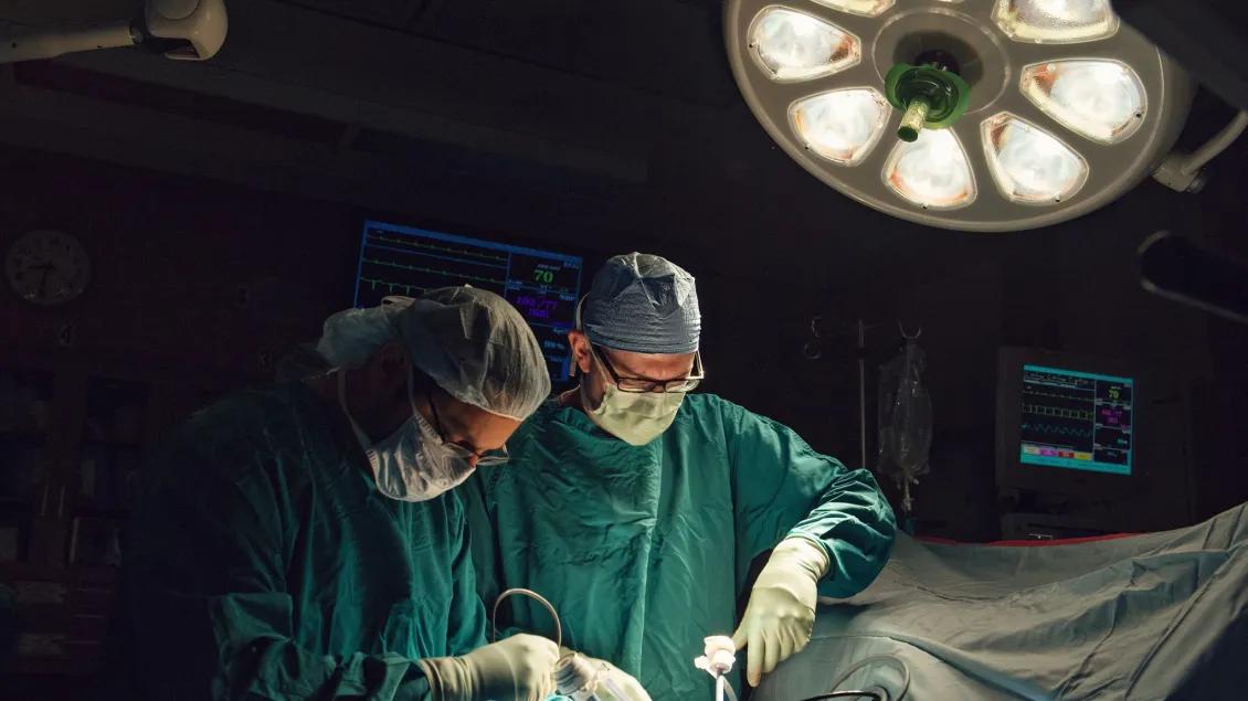 Two transplant surgeons operate under a large surgical light.