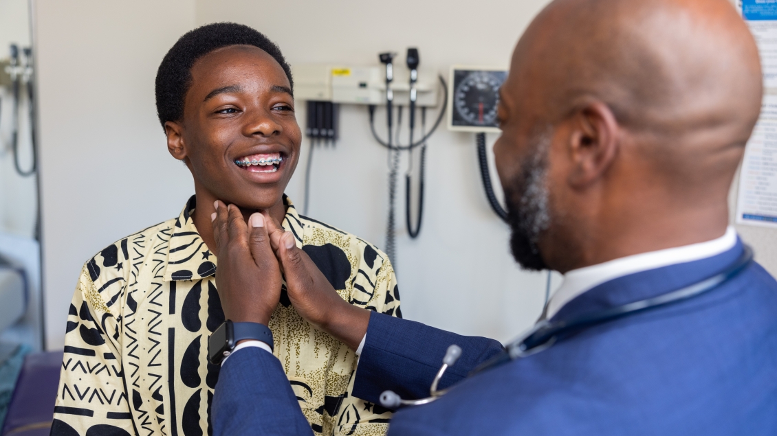 A male, African-American provider checks the lymph nodes of a young, masculine, Muslim patient