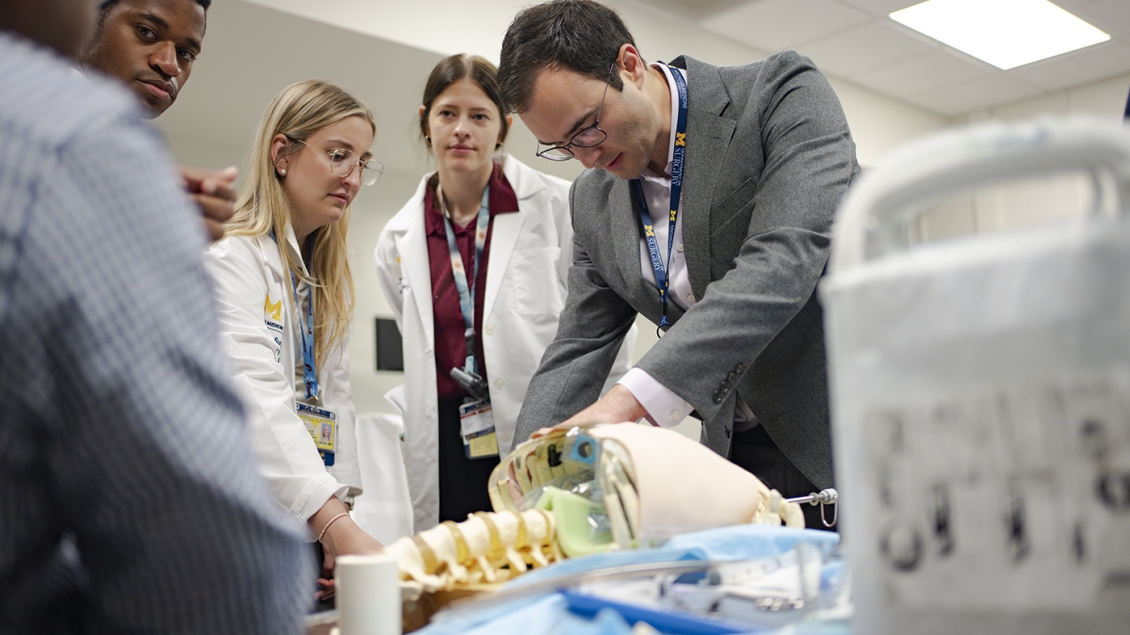 Five medical students stand around a table and work with an anatomical model torso.
