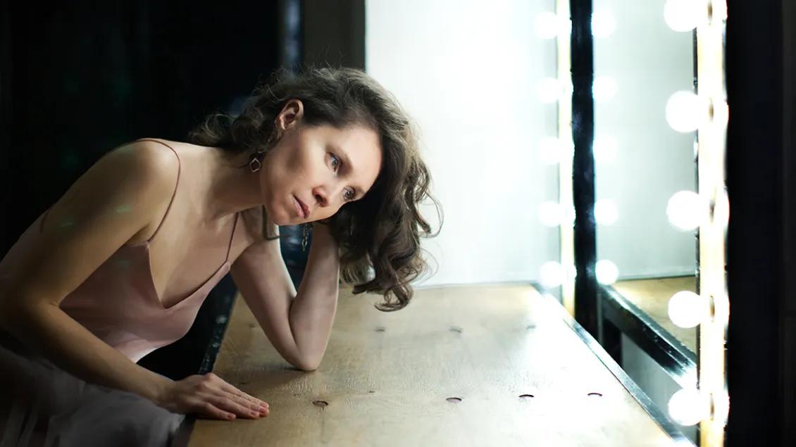 A woman who appears sad or thoughtful is seated in front of a mirror.