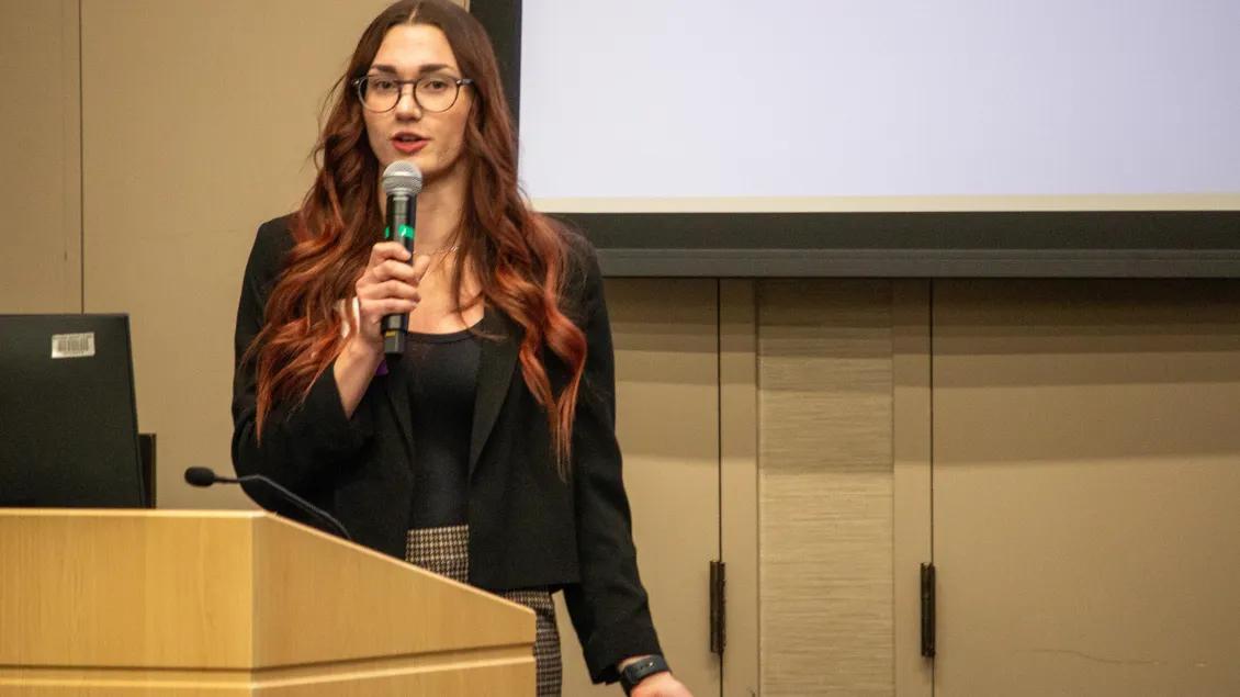 Female speaker holds microphone at podium during AHI conference