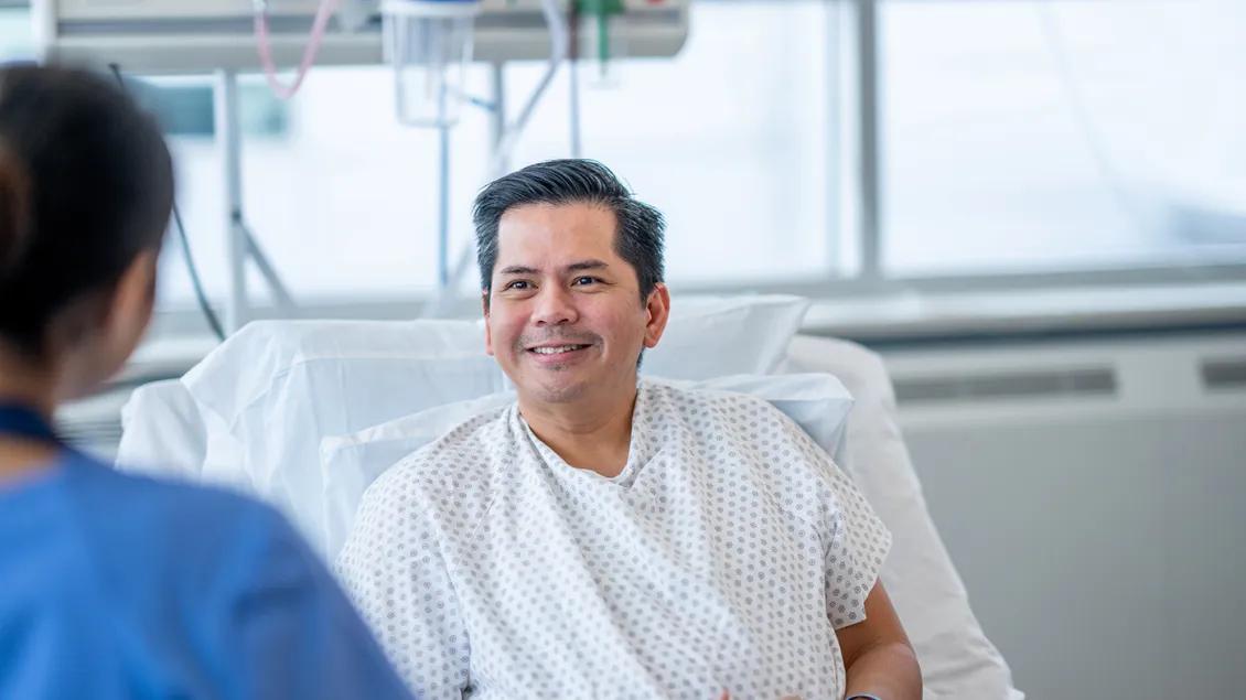 A hepatology patient sitting up in a hospital bed talks with a health care professional.