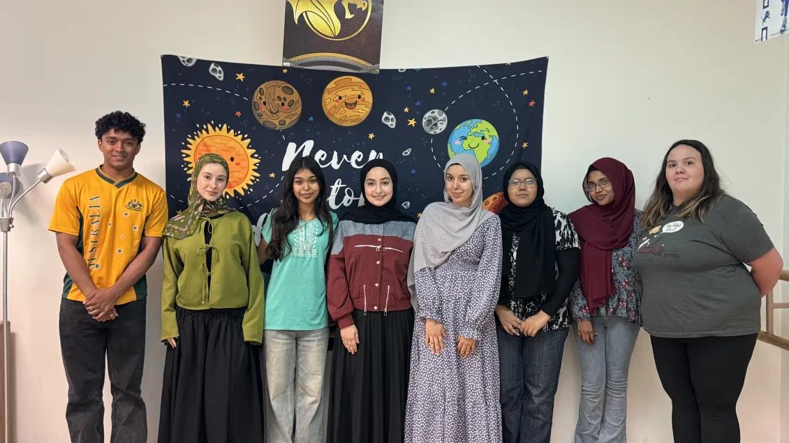 REACH members standing in front of a banner with planets.
