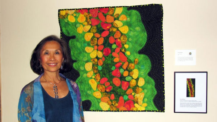 Artist standing with art quilt inspired by scientific photomicrograph