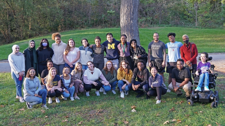 Widely diverse group of 25 students posed outside in front of a tree