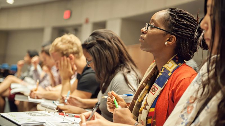 Row of students with focus on Black woman with braids wearing glasses and colorful scarf