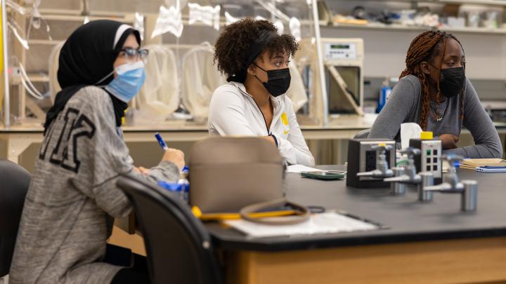 Young Black and brown women in lab wearing masks, with one wearing a hijab