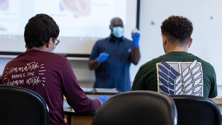 Two young men in classroom shown from behind with Black teacher in front
