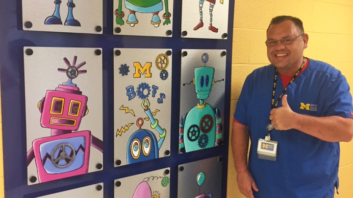 Michigan Medicine staffer smiles next to robot art mural