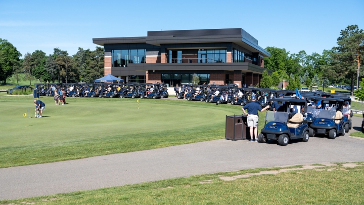 blue golf carts lined up along the side of a putting green