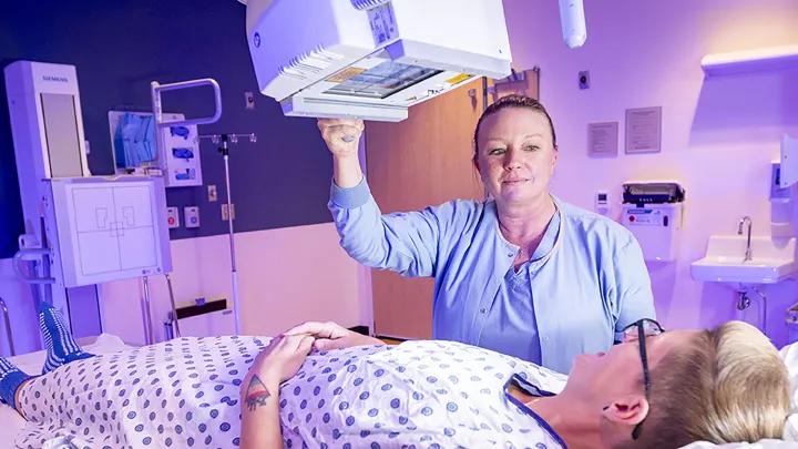 Radiologist with her hand on an overhead maching and a patient laying in front