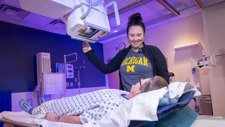 Radiology technologist with her hand on an overhead machine and a patient in front