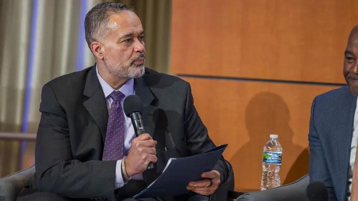 Seated man with microphone wearing a suit talking with people off camera