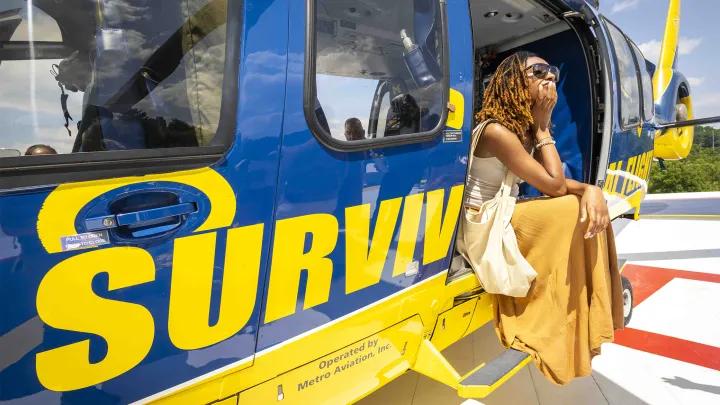 Black woman wearing gold skirt seated in doorway of Survival Flight helicopter