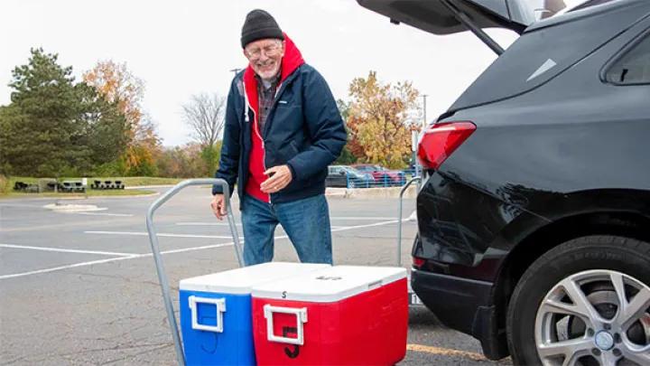 A man with two coolers are unloaded them from a black suv