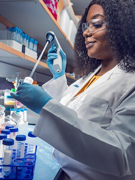 Black woman in white coat and wearing blue surgical gloves holding scientific instrument in a lab