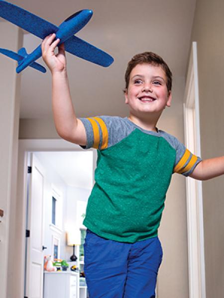 Little boy in green shirt and blue pants holding a blue toy airplane