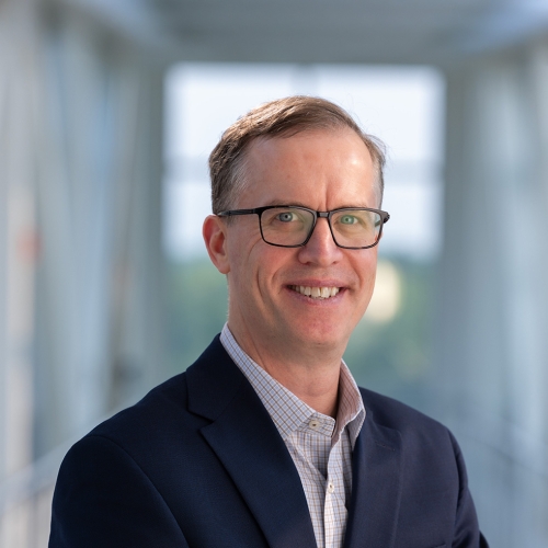 David Miller wearing glasses and blue jacket smiling  