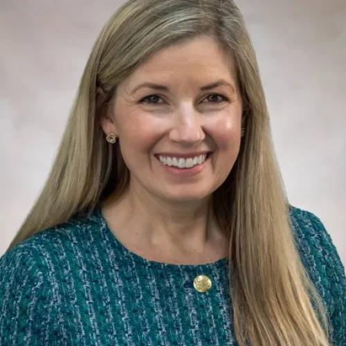 Smiling headshot of Michelle Geller. She is wearing a blue tweed button-up jacket.