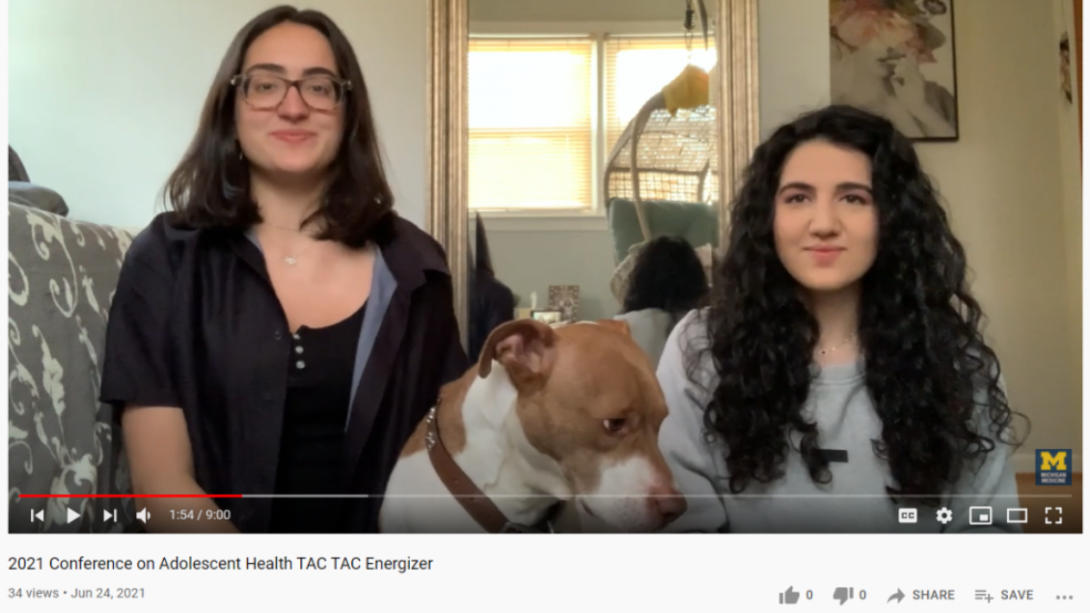 Screenshot capturing video showing two female teens and a dog seated on a sofa in a home