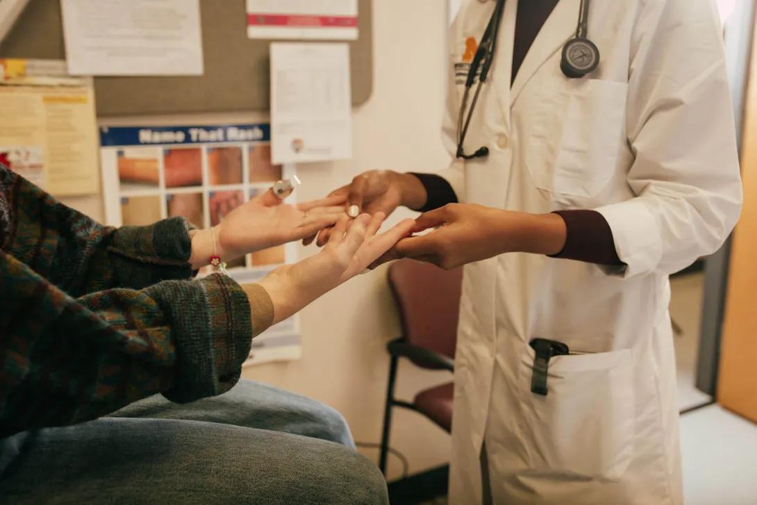 Hands and arms of white seated female patient and standing Black doctor