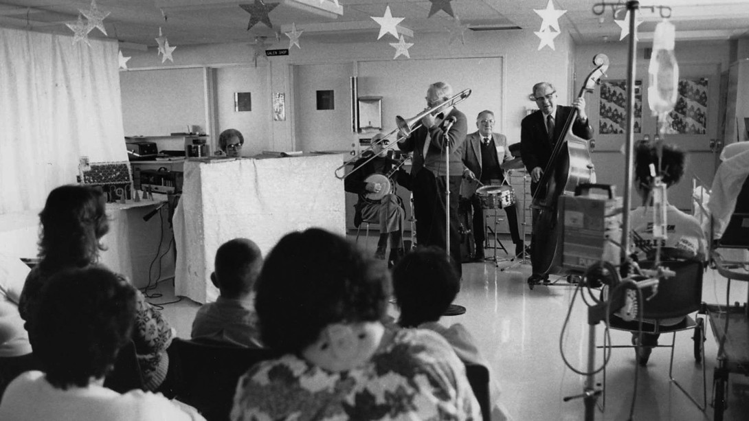 Musicians playing in hospital ward with paper stars hanging from ceiling - black & white
