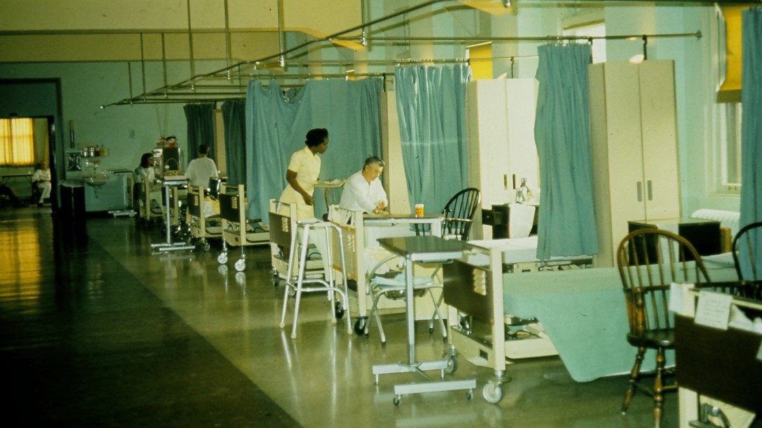 Old hospital ward with nurse wearing a dress and aqua curtains separating beds