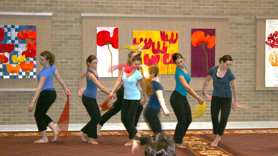 Dancers performing in front of colorful flower art on brick wall