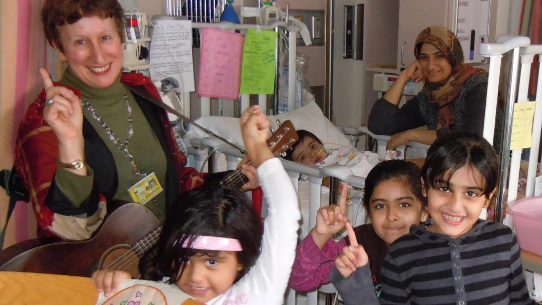 Hospital staff member smiling with mother wearing head scarf with three children and baby in hospital bed 