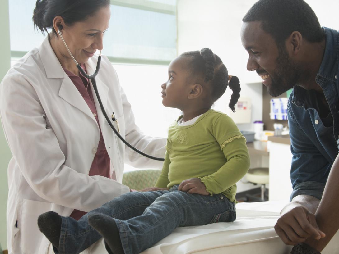 Female doctor with stethoscope examining female toddler while smiling father looks on