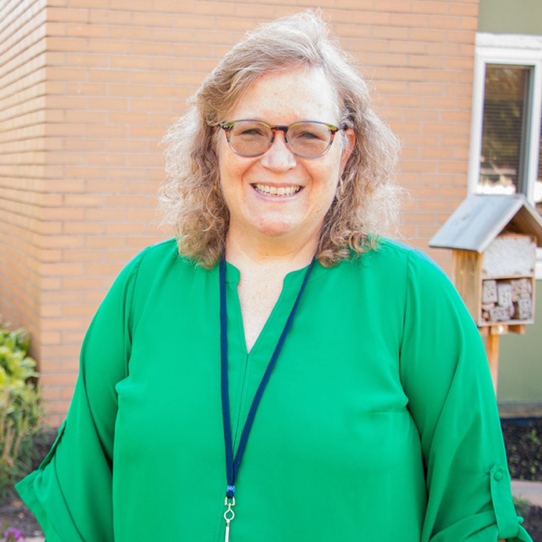 Smiling white woman with blond hair and glasses wearing green dress standing outside