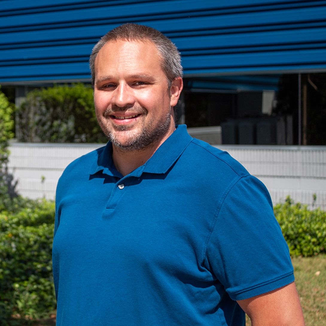 White man with beard standing outside smiling and wearing blue polo shirt 