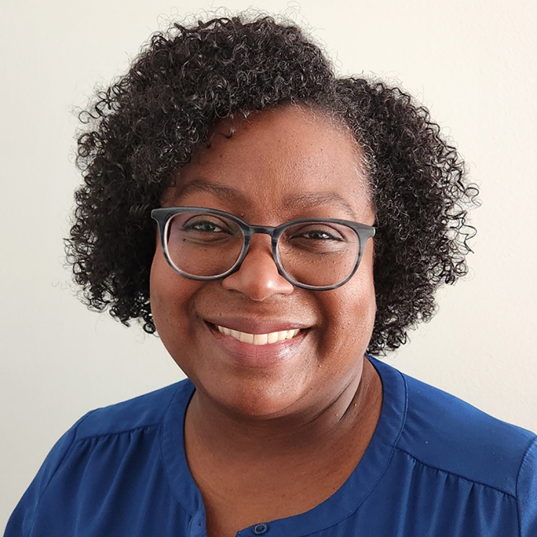 Smiling black woman with hair parted on the side wearing glasses and blue dress 