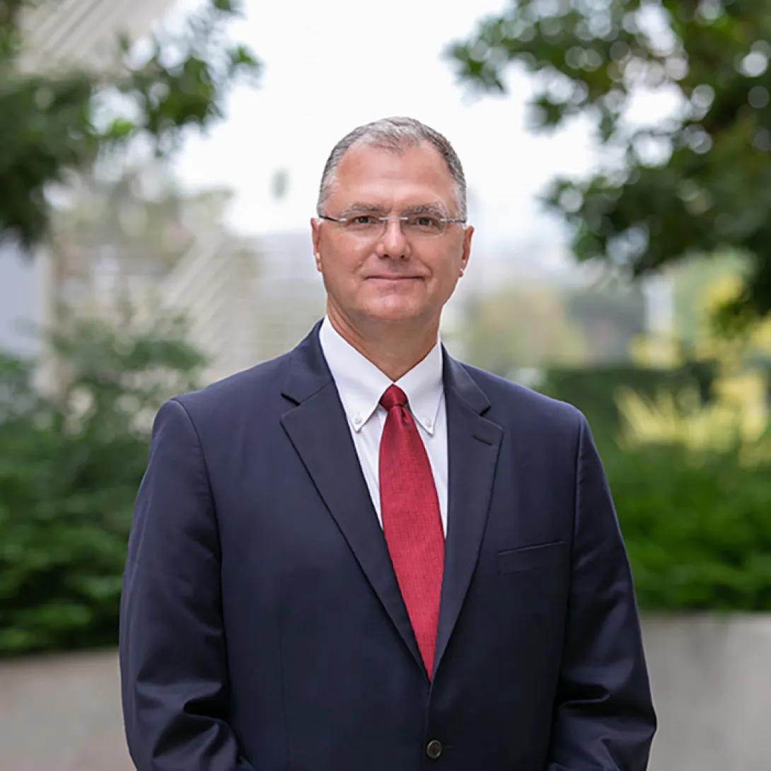 Head and shoulders shot of Eric Strucko, wearing glasses and a navy blue suit with red tie