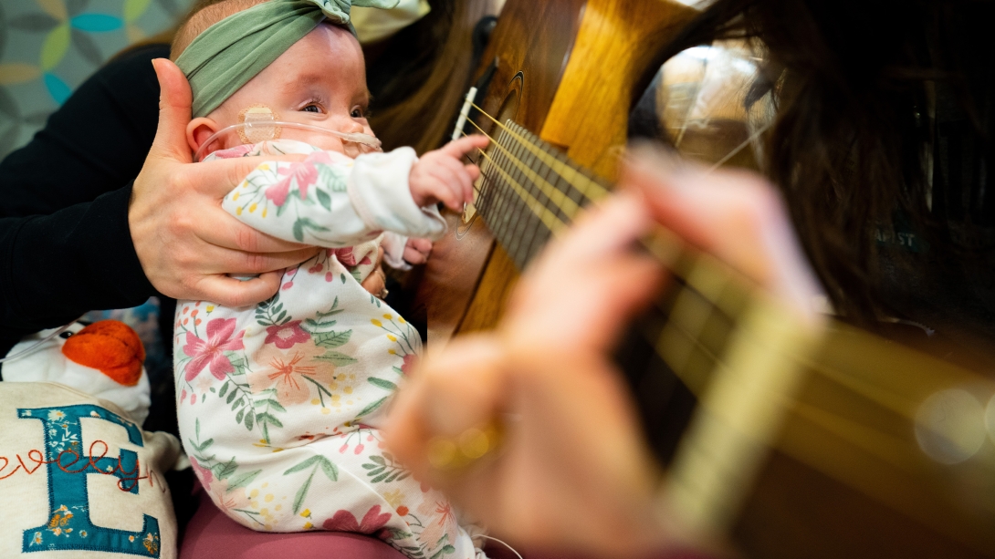 baby holding guitar with two adults close up snuggled