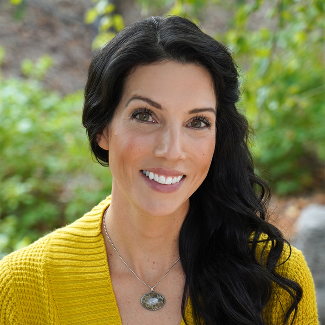 Head and shoulders shot of Kali Lake, white woman with long black hair smiling and wearing gold sweater with silver necklace