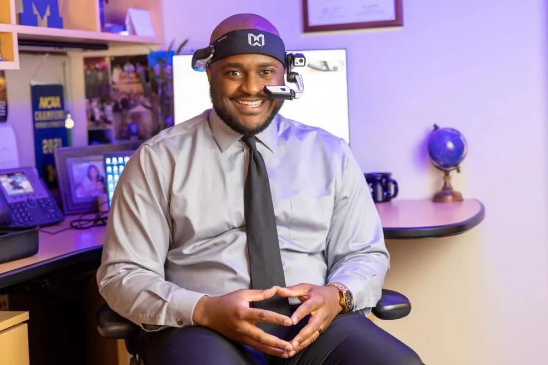 man in shirt and tie smiling at camera in office with headset on