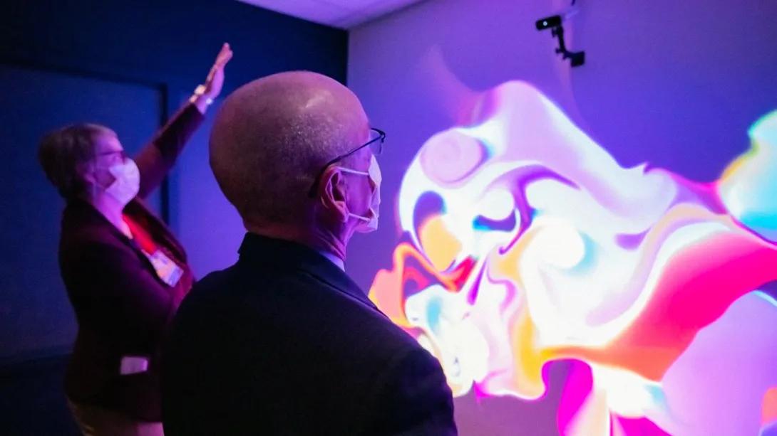 two people looking at wall and moving hand with mix of colors on wall dark room